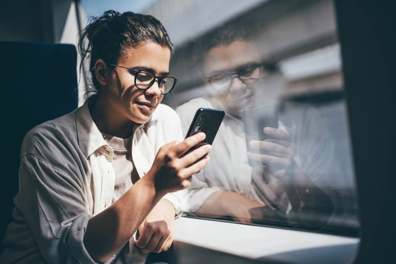 Junge Frau im Zug schaut lächelnd auf ihr Smartphone – Deutschlandticket mit TicketPlus+ einfach per App nutzen